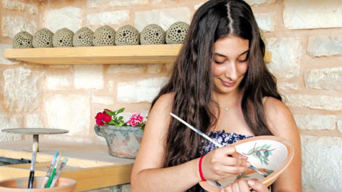 Μια νέα τεχνίτρια ζωγραφίζει προσεκτικά κεραμικά, διατηρώντας την πλούσια παράδοση της κρητικής χειροτεχνίας.